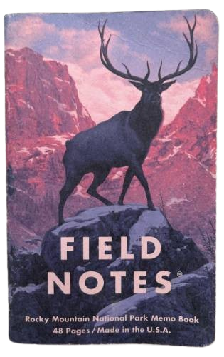 small notebook with a purple cover of the rocky mountains. and a huge ass deer